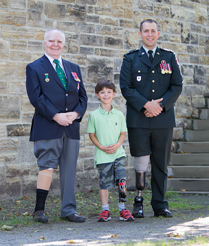 A young male leg amputee smiles and stands in between two male war amputee veterans.