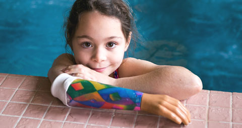 Une enfant amputée portant son bras artificiel pour l’eau dans une piscine.