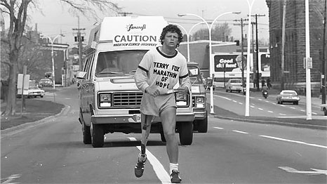 Terry Fox wearing an artificial leg, running on the road with a van following behind him.
