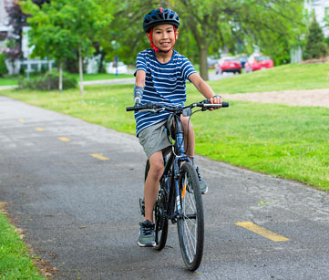 A young male arm amputee rides his bike on a park pathway.