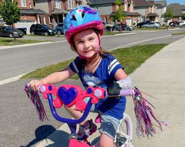 A young female arm amputee rides her pink bike down a sidewalk.