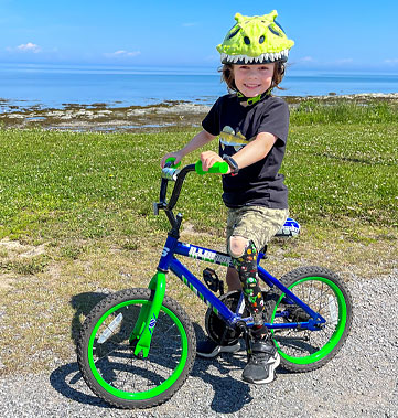 A young male multiple amputee rides his bike near the ocean.