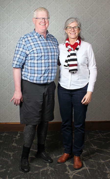 A adult male double foot amputee stands beside an adult female arm amputee at a hotel.