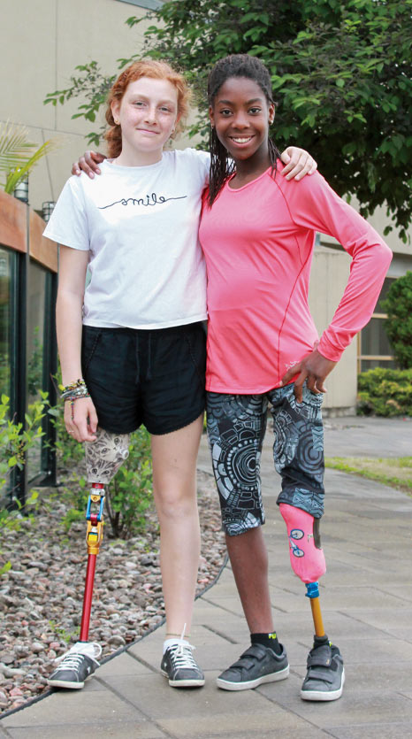 Deux jeunes filles amputées d’une jambe posent dans une allée.