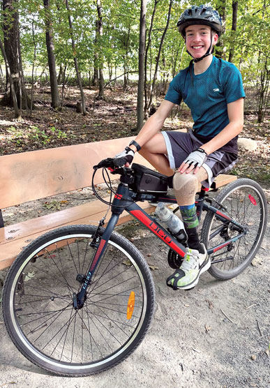 A young adult male leg amputee rides a bike on a forest path.