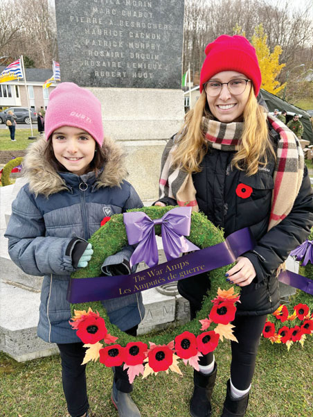 A young female amputee and a young adult female amputee hold a wreath together in front of a cenotaph.