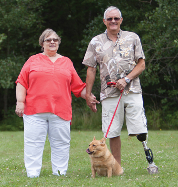 Un homme âgé amputé d’une jambe se promène avec sa femme et son petit chien en lisière de forêt.