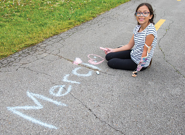 Une jeune fille amputée portant un bras artificiel écrit le mot « merci » à la craie sur le trottoir.