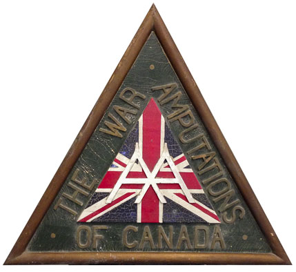 Le logo de l’Association des Amputés de guerre de 1939, sculpté sur une plaque triangulaire en bois.