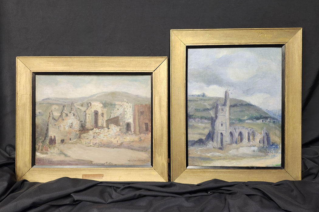 Two gold-framed paintings of ruined landscapes, one horizontal and one vertical, are propped up on black fabric.