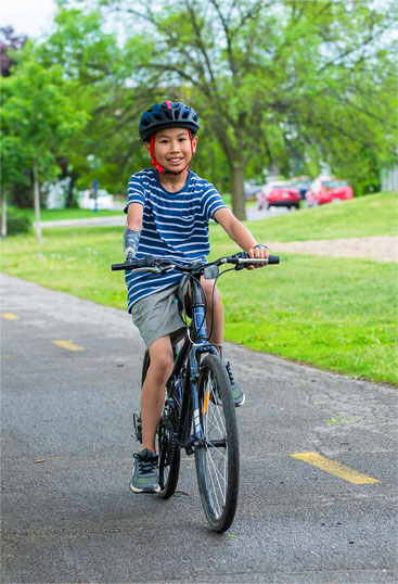 Un jeune garçon amputé fait du vélo à l’aide de son bras artificiel et d’un dispositif fixé sur le guidon.