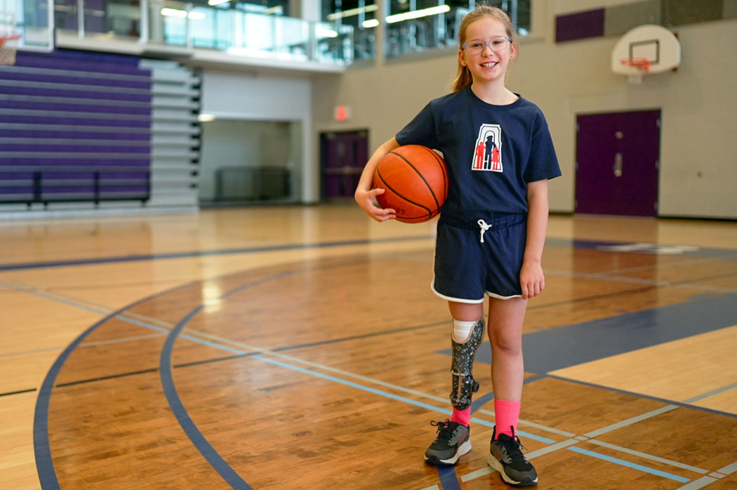 Une jeune fille ayant une amputation à la jambe tient un ballon de basketball dans un gymnase.