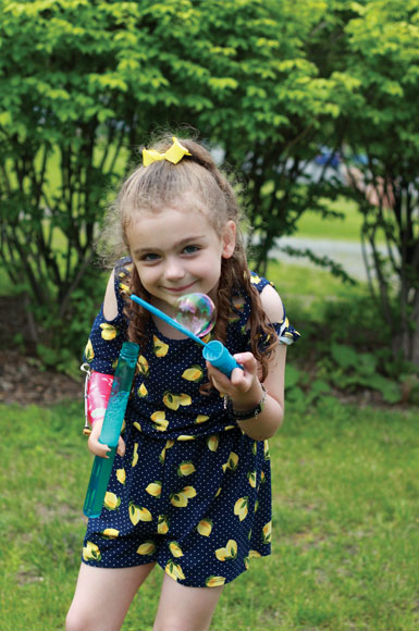 Sarah, une jeune amputée au bras, tient un tube de savon à bulles avec sa prothèse et une baguette à bulles dans l’autre main.