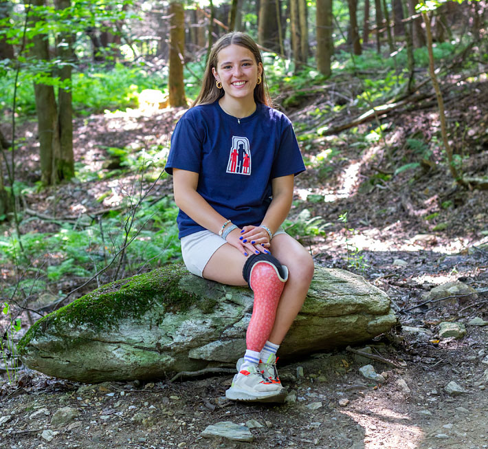 Florence, qui est amputée d’une jambe, est assise sur une roche dans une forêt.