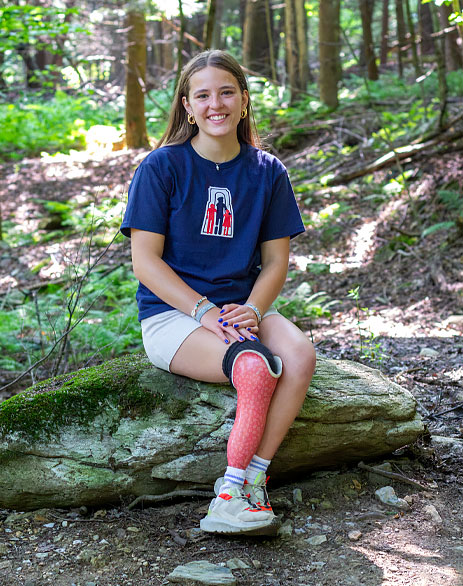 Florence, qui est amputée d’une jambe, est assise sur une roche dans une forêt.