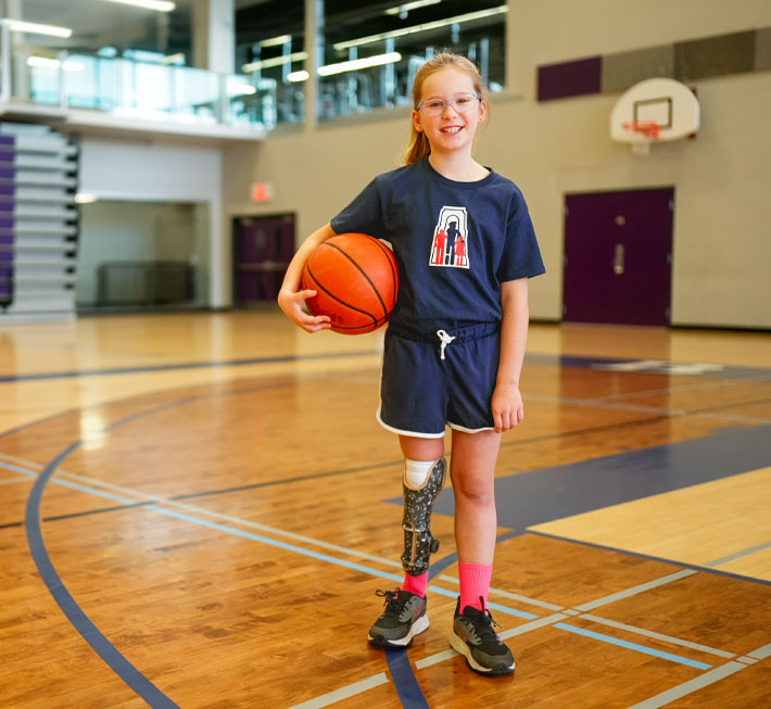 Jeanne, une jeune fille amputée d’une jambe, tient un ballon de basketball dans un gymnase.