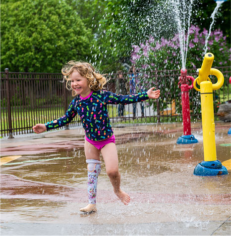 A young female leg amputee plays at a park's splash pad.