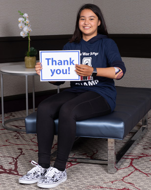 A young amputee girl wearing a prosthetic arm holds a sign with “thank you!” written on it.