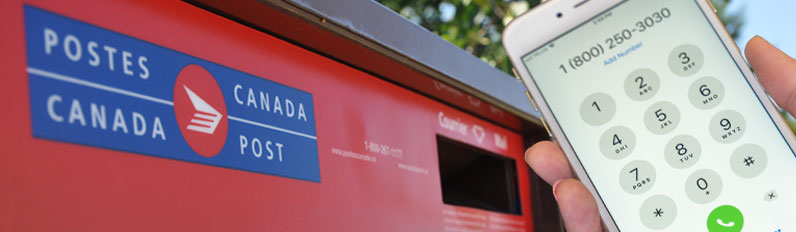 A person holds a cell phone with the War Amps phone number 1 800 250-3030 displayed in front of a Canada Post mailbox.